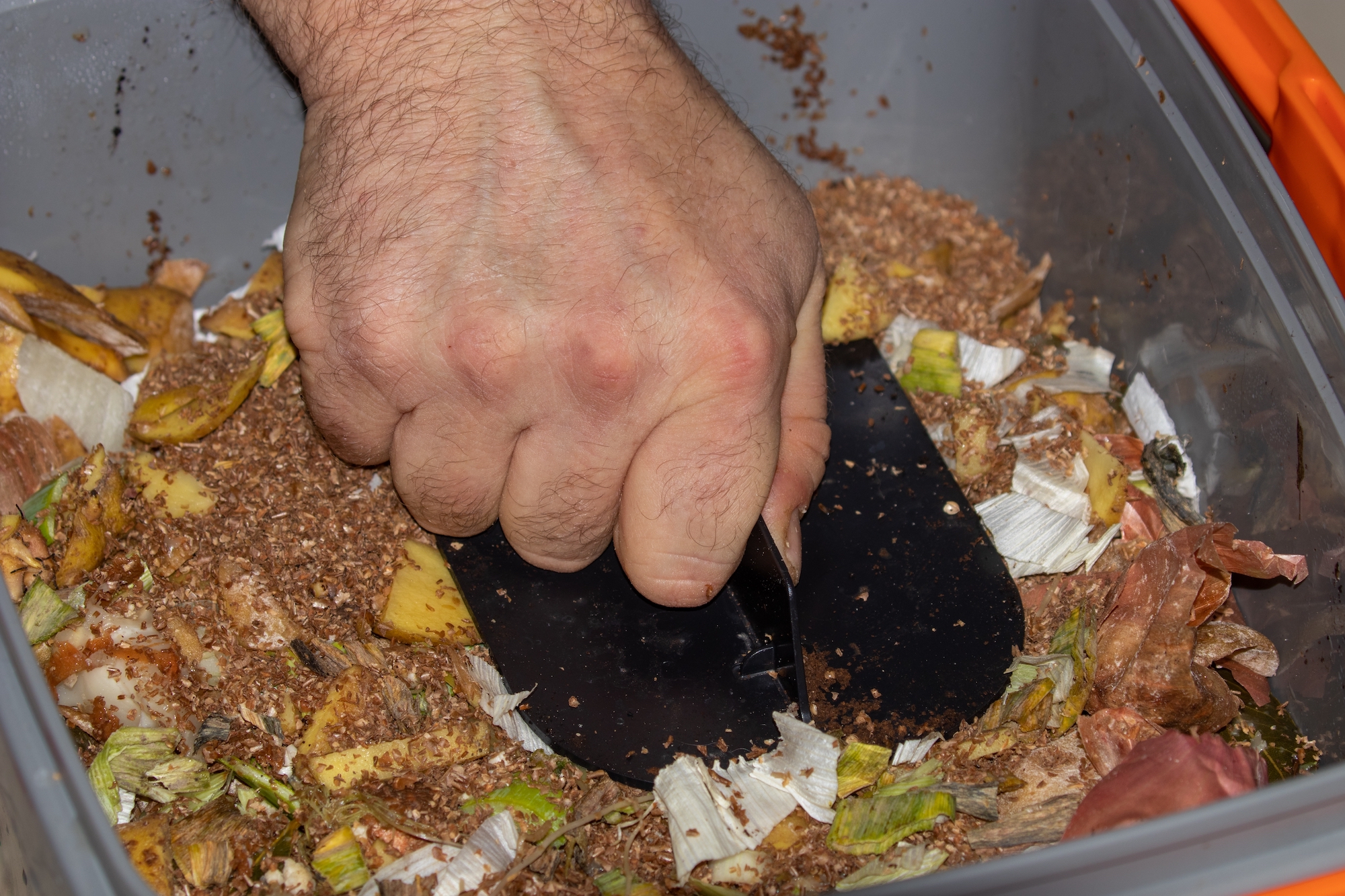 Male handing pressing down food scraps in a bokashi composter.